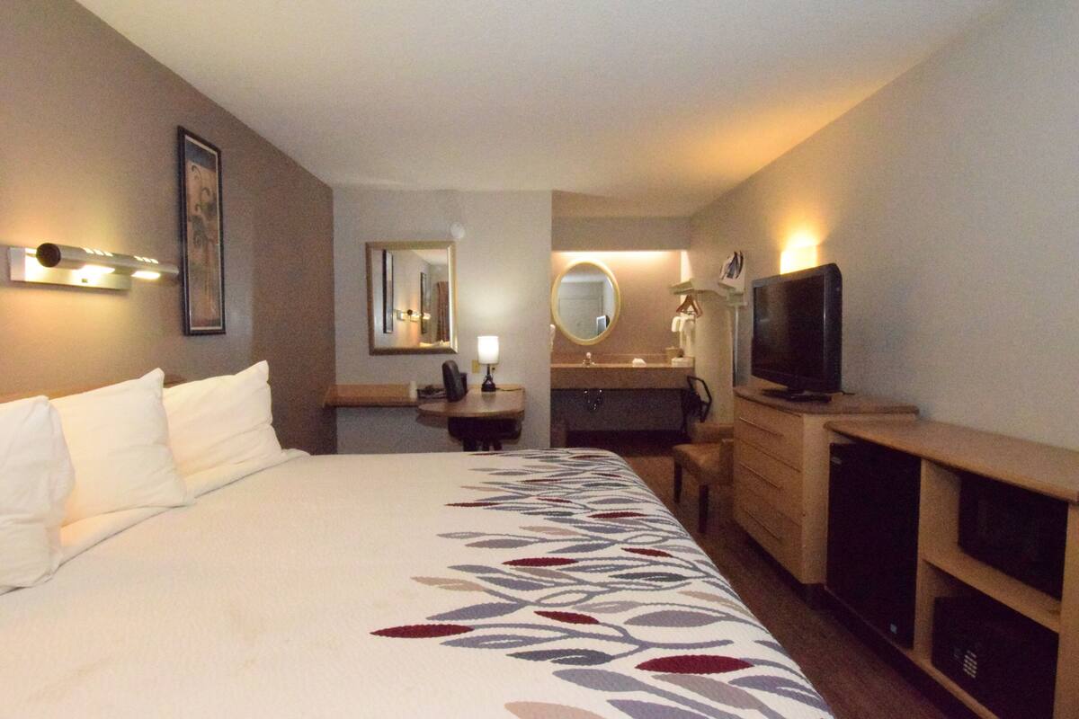 Une chambre d’hôtel avec un grand lit, un bureau, une télévision, un miroir et une salle de bain.