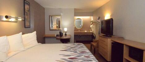 A hotel room with a large bed, a desk, a television, a mirror, and a bathroom.