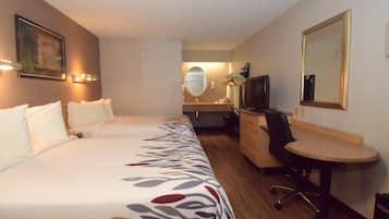Une chambre d’hôtel avec deux lits, un bureau, une chaise, une télévision et un miroir. On aperçoit également une salle de bain au fond.