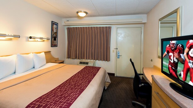 Habitación de hotel con cama, televisión, escritorio y ventana con cortinas.