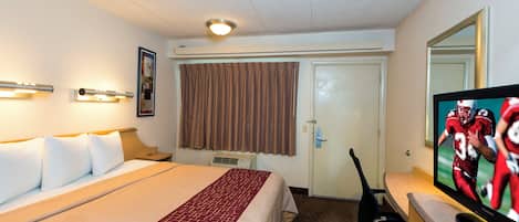 A hotel room with a bed, a television, a desk, and a window with curtains.