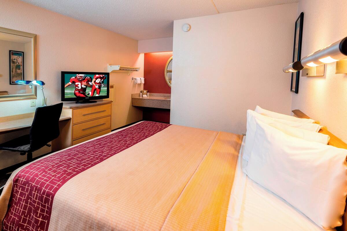 Une chambre d’hôtel comprenant un lit, un bureau avec un ordinateur, une télévision et un miroir.