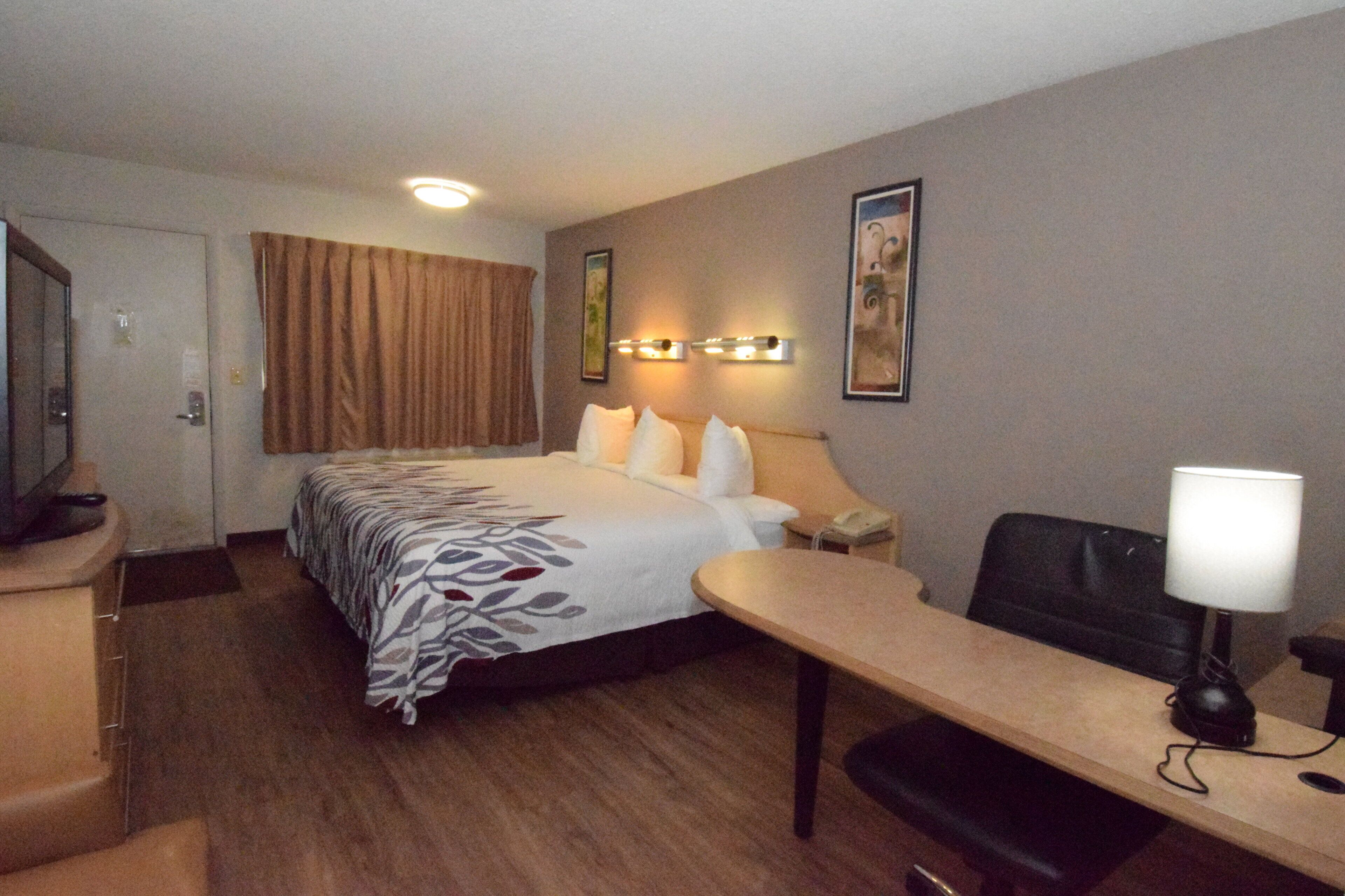 Een hotelkamer met een bed, nachtkastje, lamp, stoel en bureau.