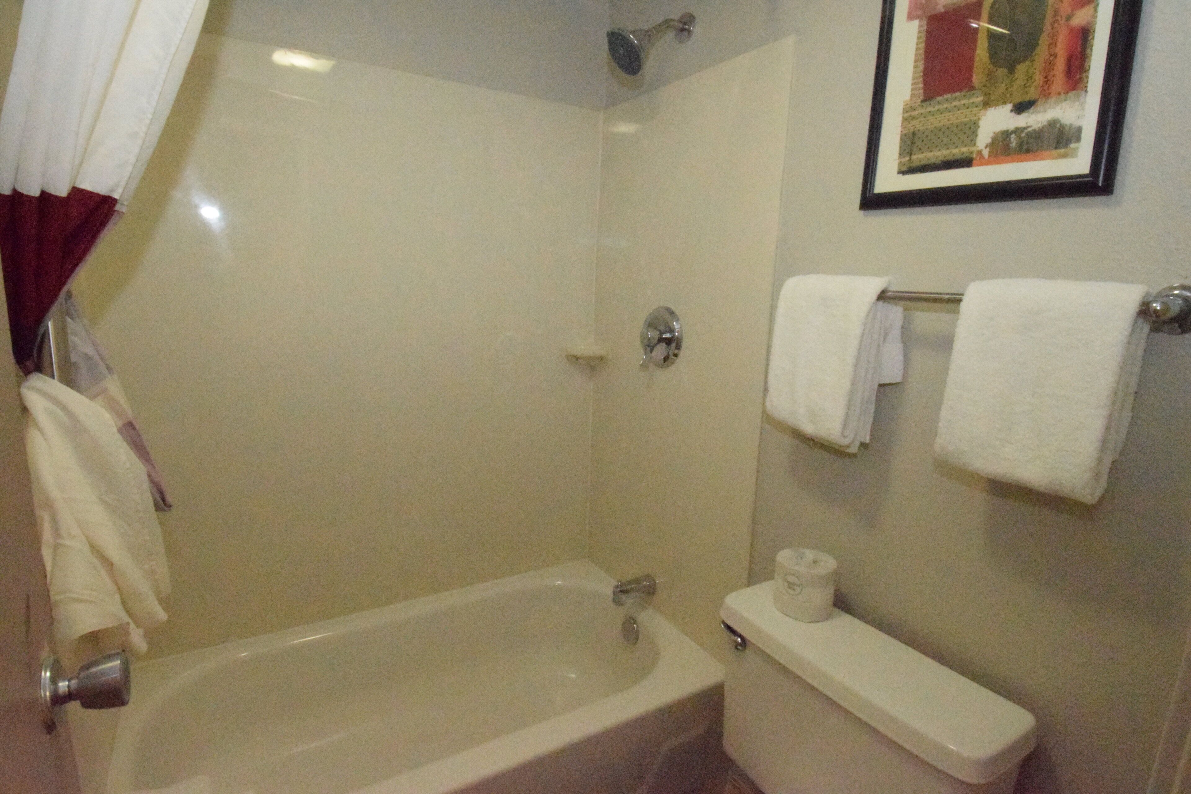 A bathroom with a bathtub, toilet, and a shower. There are towels hanging on a rack.
