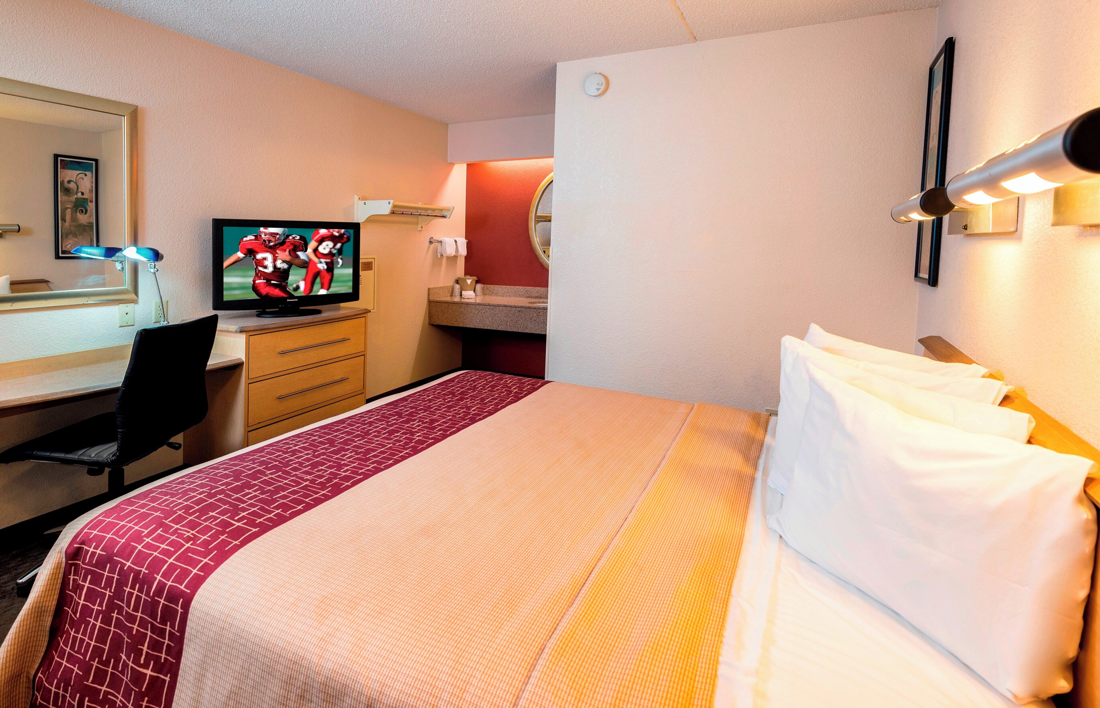 A hotel room with a bed, a desk with a computer, a television, and a mirror.