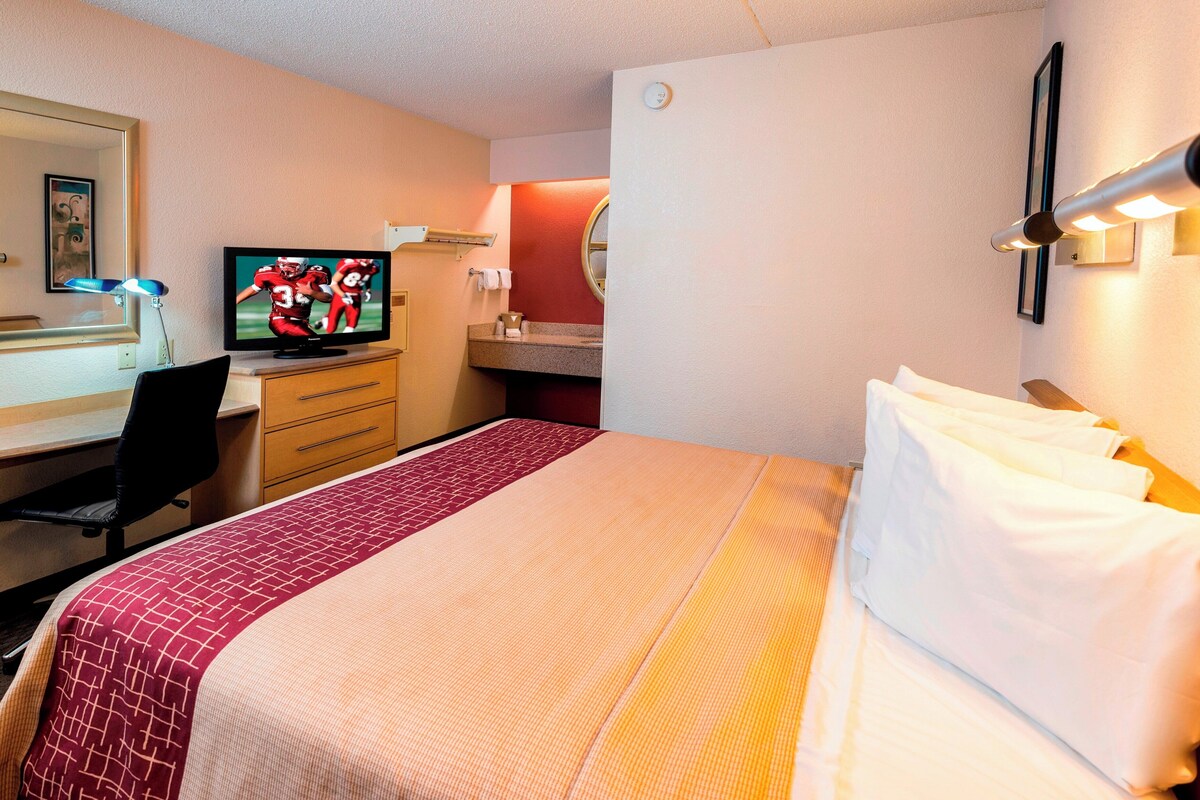 A hotel room with a bed, a desk with a computer, a television, and a mirror.