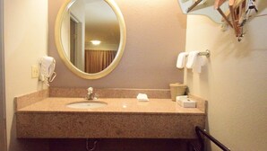 Un baño con lavamanos de granito, un espejo redondo, un secador de pelo y dispensador de toallas.