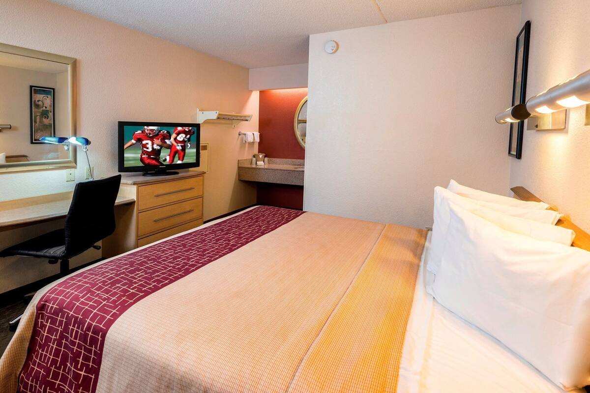 Une chambre d’hôtel comprenant un lit, un bureau avec un ordinateur, une télévision et un miroir.