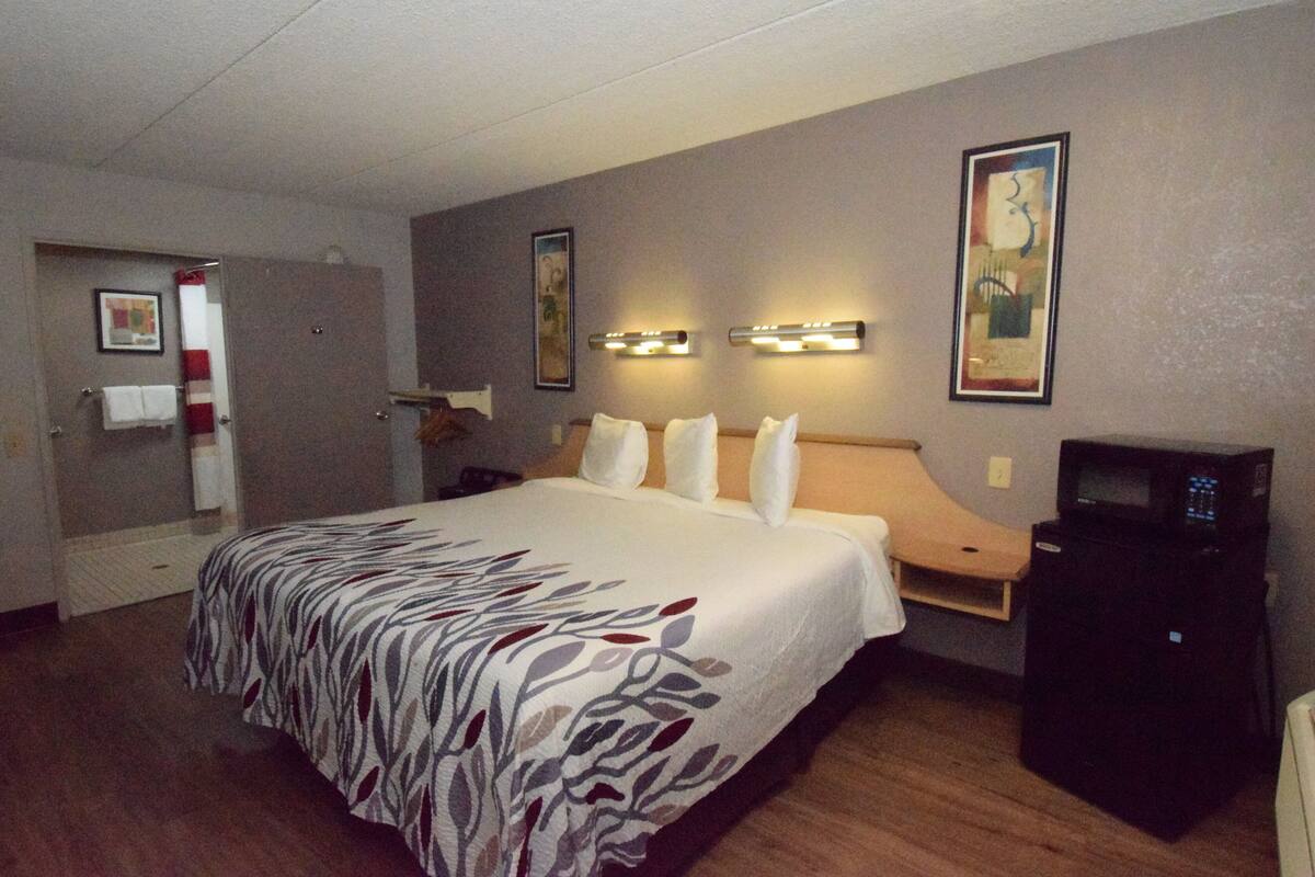 Et hotelværelse med en stor seng, et skrivebord med en computer og en mikrobølgeovn.