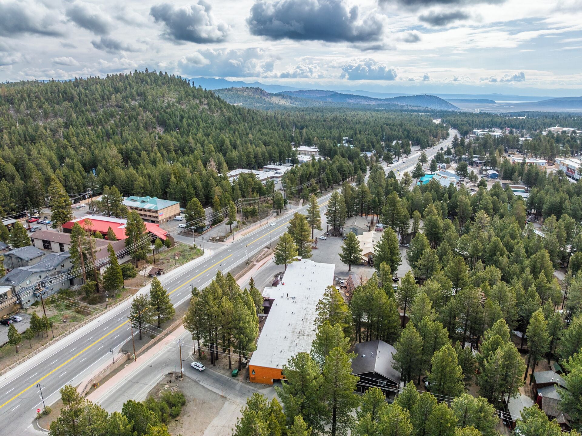 An aerial view of a town with a main road, buildings, and a forested area.
