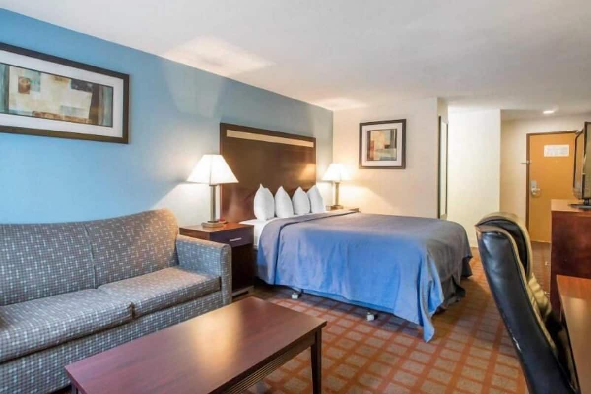 A hotel room with a bed, a sofa, a table, and two lamps.