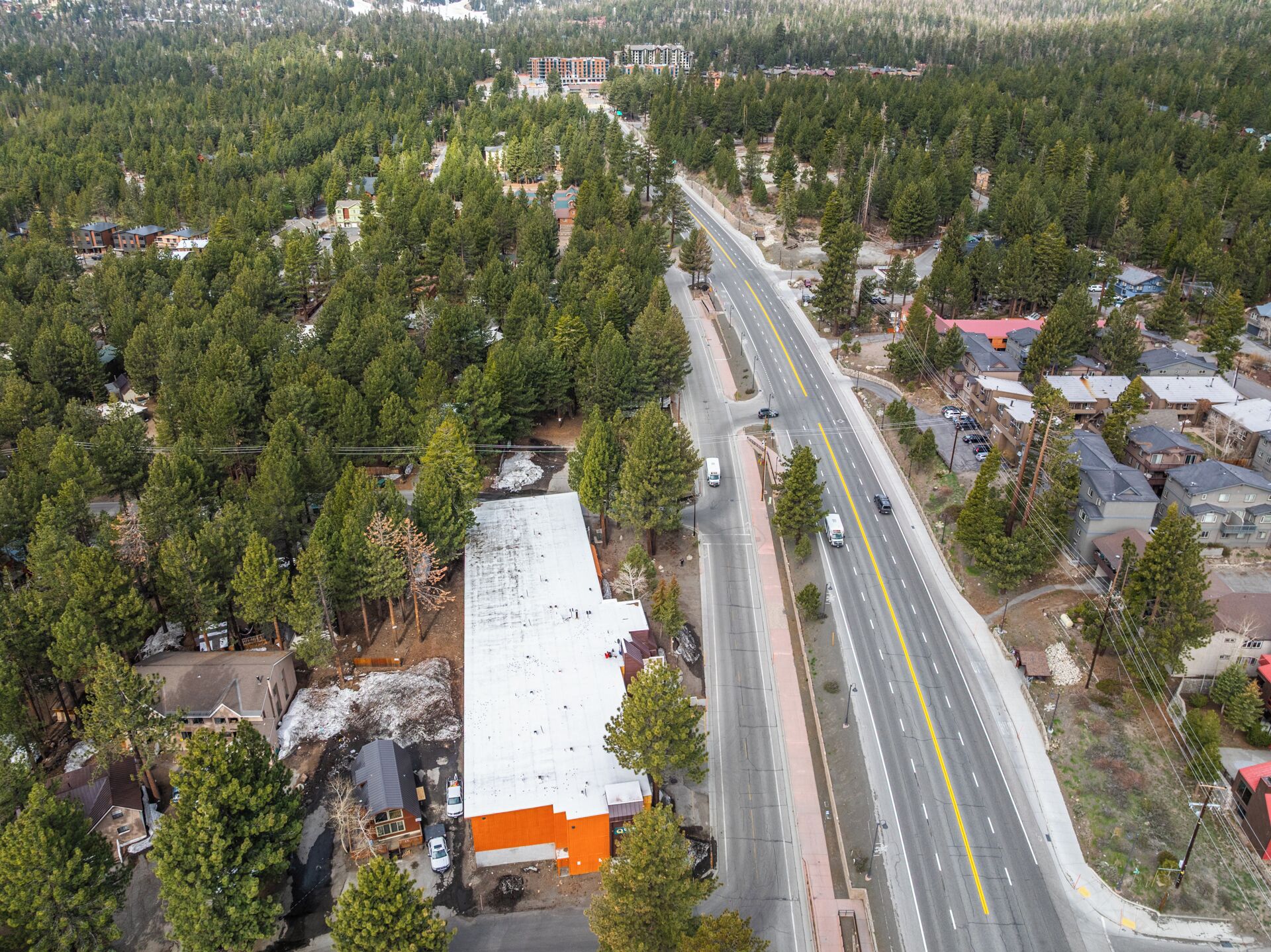 An aerial view of a residential area with a main road, houses, and a large building with a white roof.