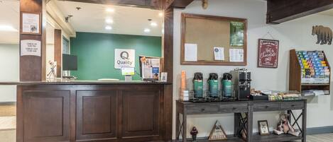 A hotel reception area with a wooden reception desk, a green wall, and a bulletin board.
