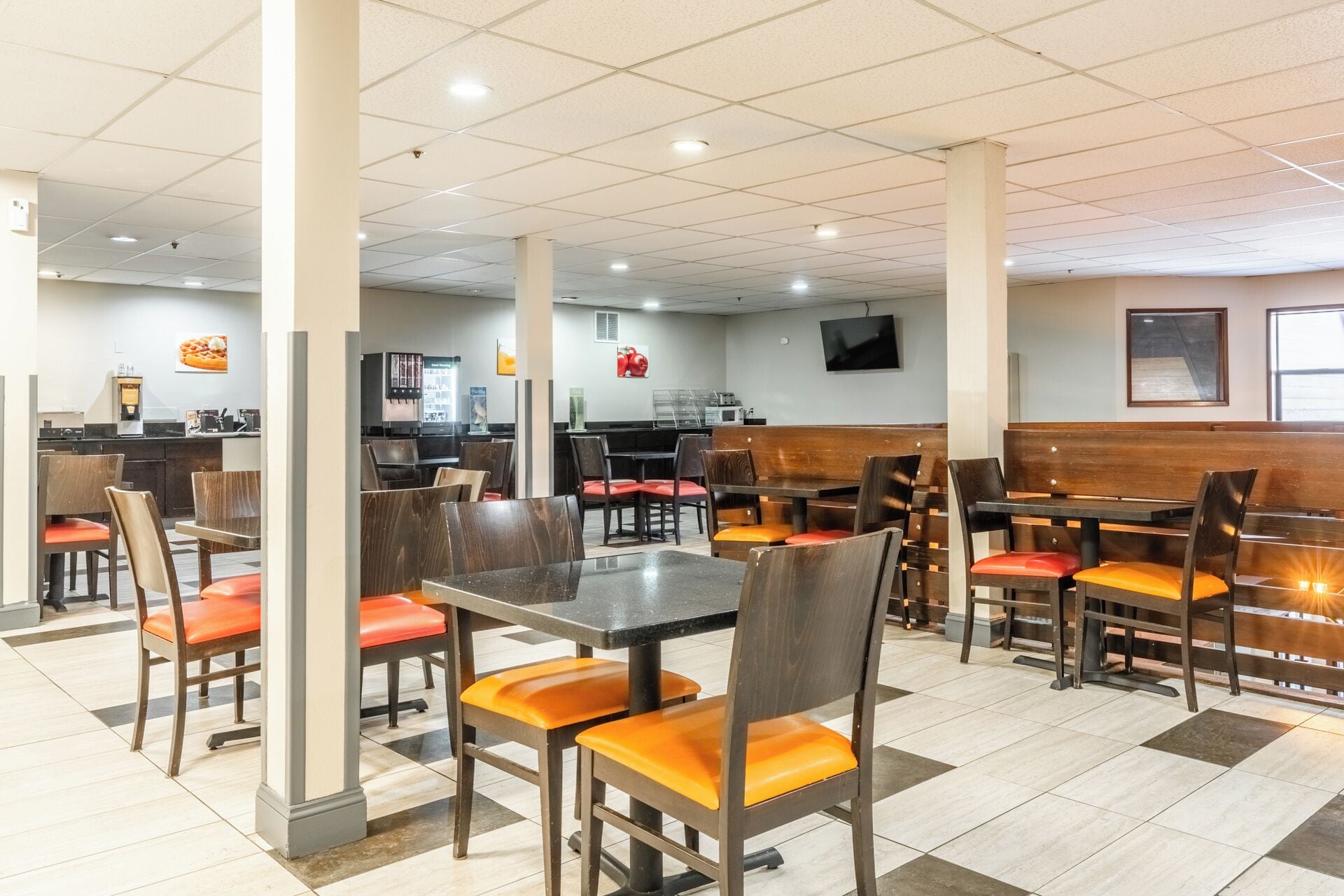 Un restaurante con cabinas y mesas, una zona de cocina y un televisor de pantalla plana en la pared.
