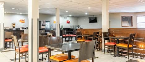 Un restaurante con cabinas y mesas, una zona de cocina y un televisor de pantalla plana en la pared.