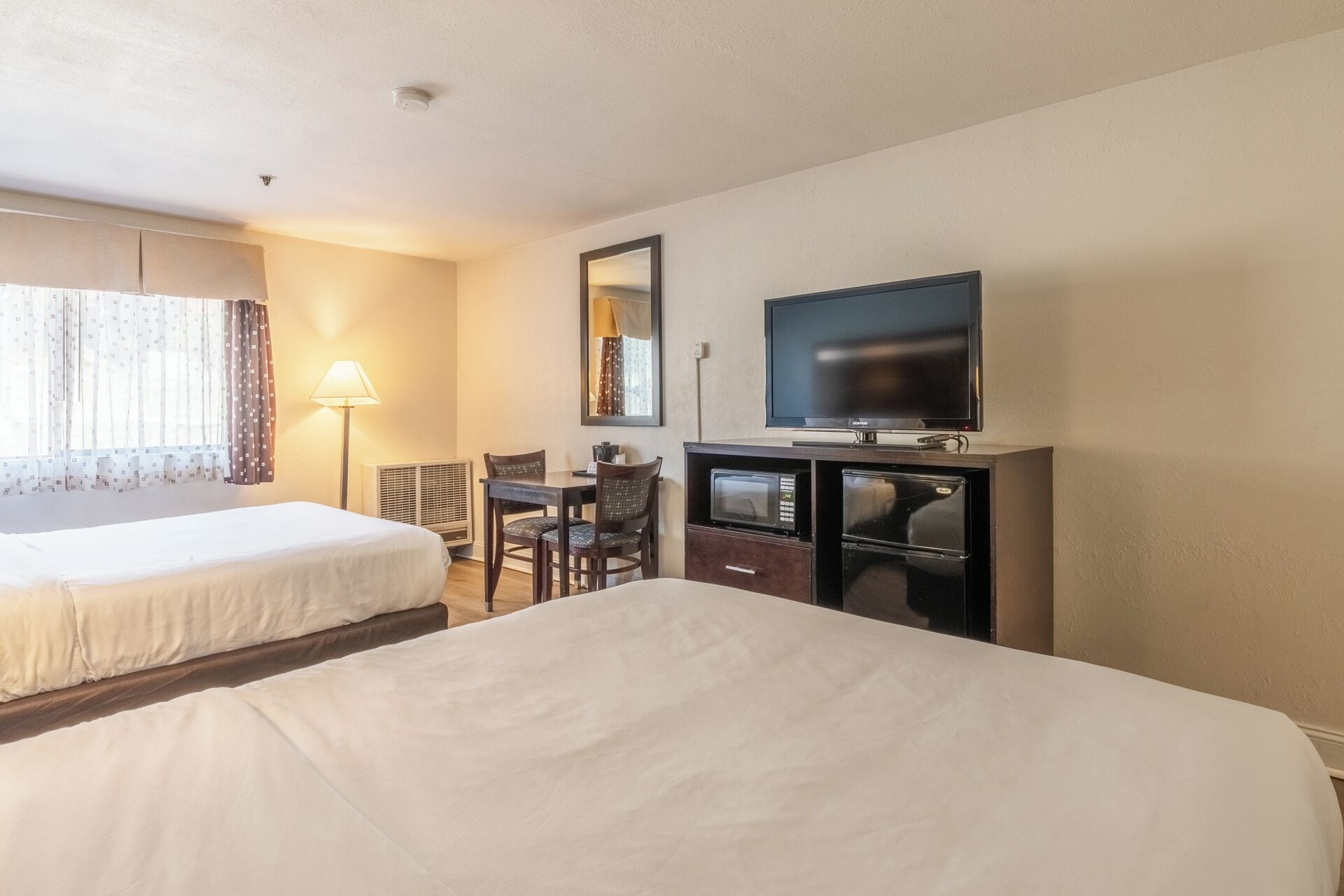 A hotel room with two beds, a desk, a chair, a television, and a microwave.