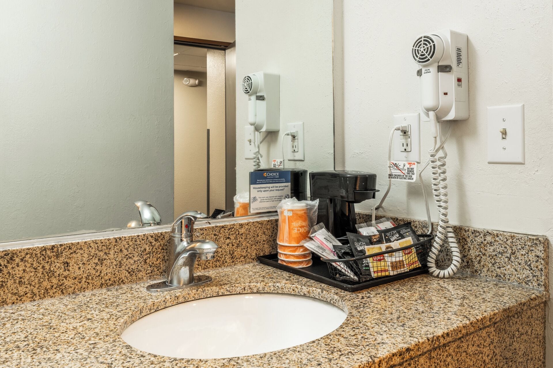 Een hotelbadkamer met een granieten aanrecht, een wastafel, een spiegel, een haardroger, een koffiezetapparaat en toiletartikelen.