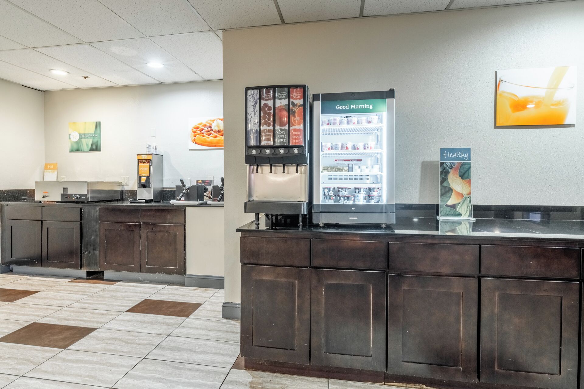 A hotel reception area with a coffee machine, a juice dispenser, and a refrigerator.