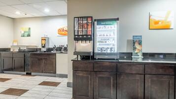 A hotel reception area with a coffee machine, a juice dispenser, and a refrigerator.