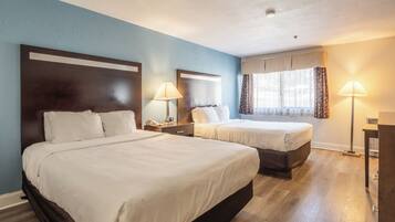 A hotel room with two beds, a nightstand with a lamp, a window with curtains, and a ceiling light.