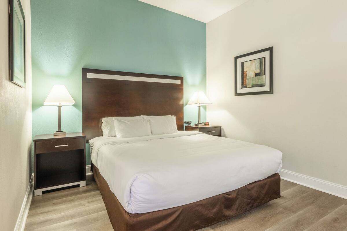 A hotel room with a bed, two bedside tables with lamps, a nightstand, and a framed picture on the wall.