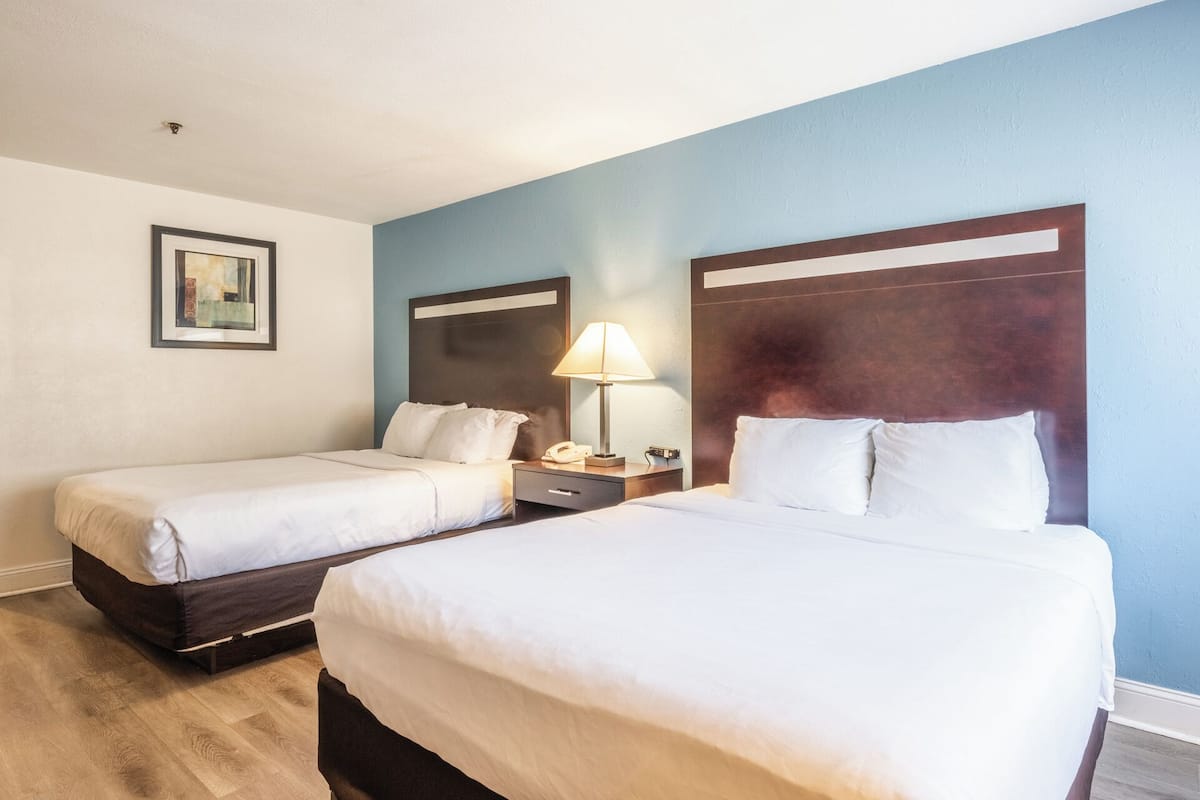 A hotel room with two beds, a nightstand with a lamp, and a framed picture on the wall.