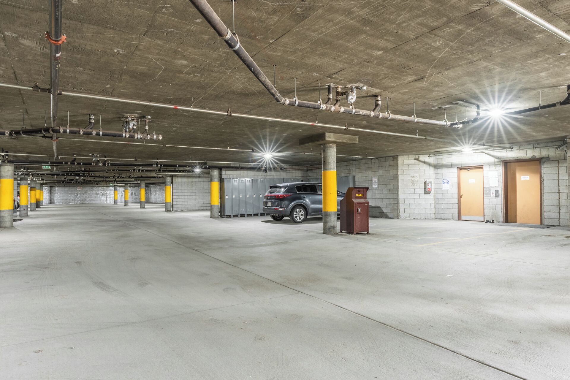 Un parking à plusieurs niveaux, avec des piliers en béton, une poubelle et un véhicule stationné au centre.