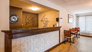A reception area with a wooden reception desk, a wall-mounted clock, and a decorative branch sculpture. There is a seating area with chairs and a table, and a framed picture on the wall. - Best Western Galena Inn & Suites (Galena)