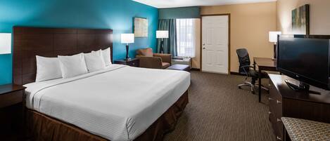 A hotel room with a large bed, a desk with a flat-screen TV, a chair, and a desk lamp.