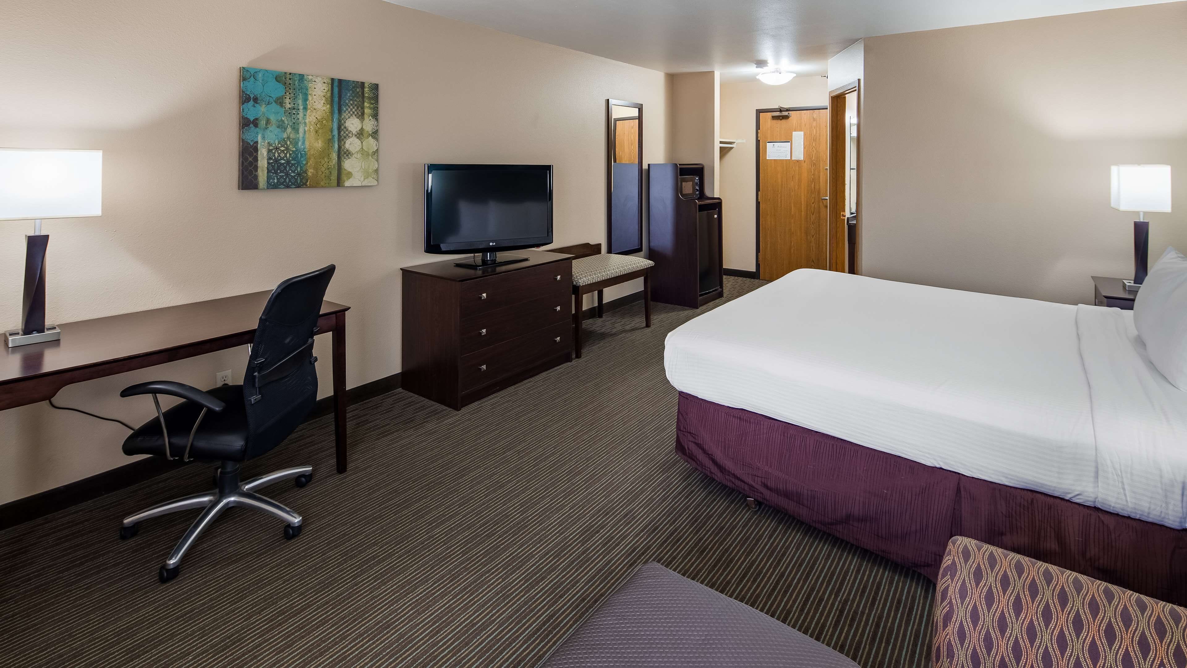 Une chambre d’hôtel avec un lit, un bureau, une chaise, une télévision et un tableau au mur.