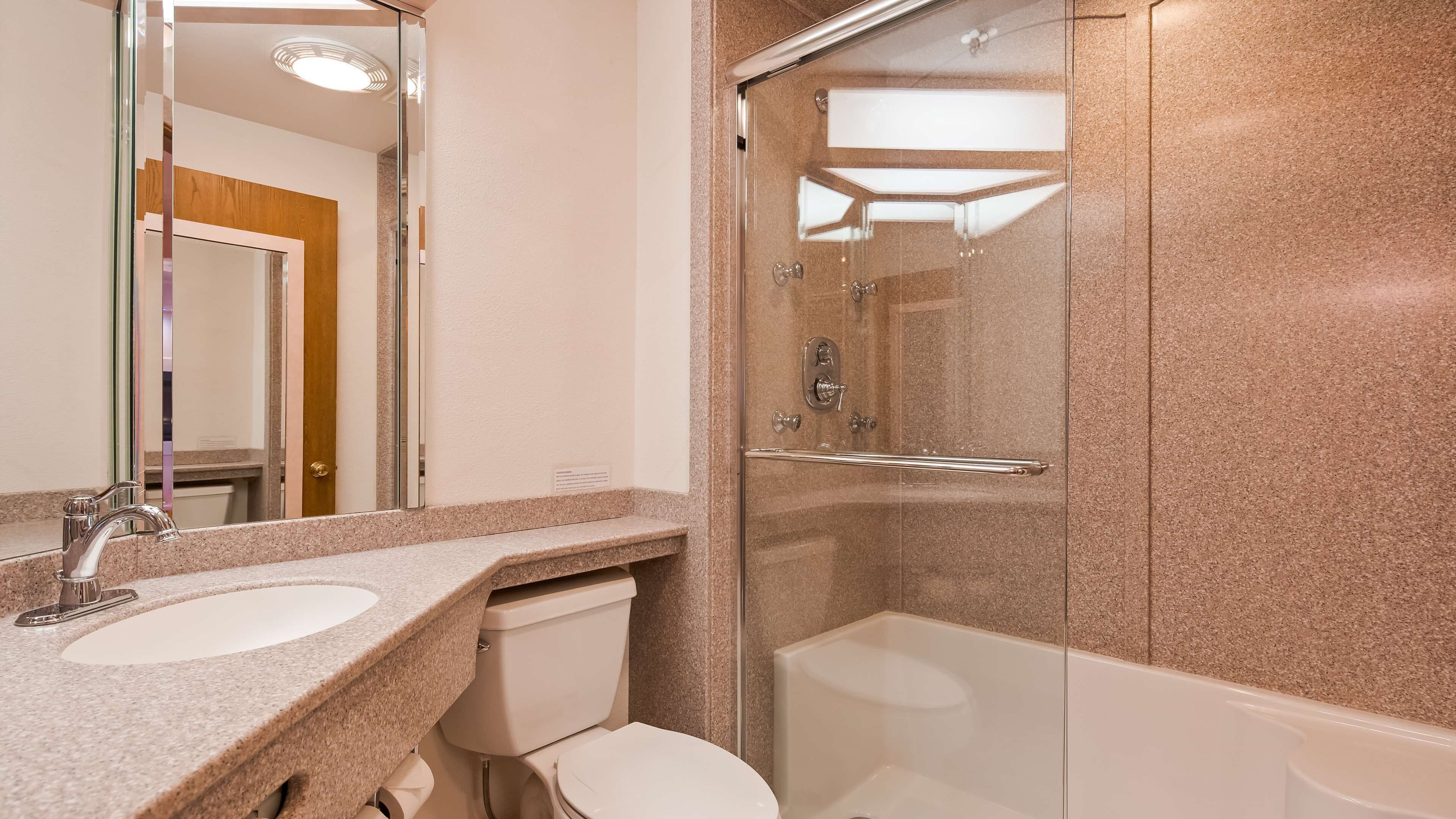 A modern bathroom with a granite countertop, a glass-enclosed shower, and a white toilet.