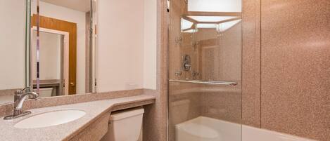 A modern bathroom with a granite countertop, a glass-enclosed shower, and a white toilet.