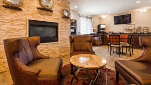 A modern living room with leather armchairs, a round coffee table, a flat-screen TV mounted on a brick wall, and a kitchen area with a coffee machine and breakfast bar. - Best Western Galena Inn & Suites (Galena)