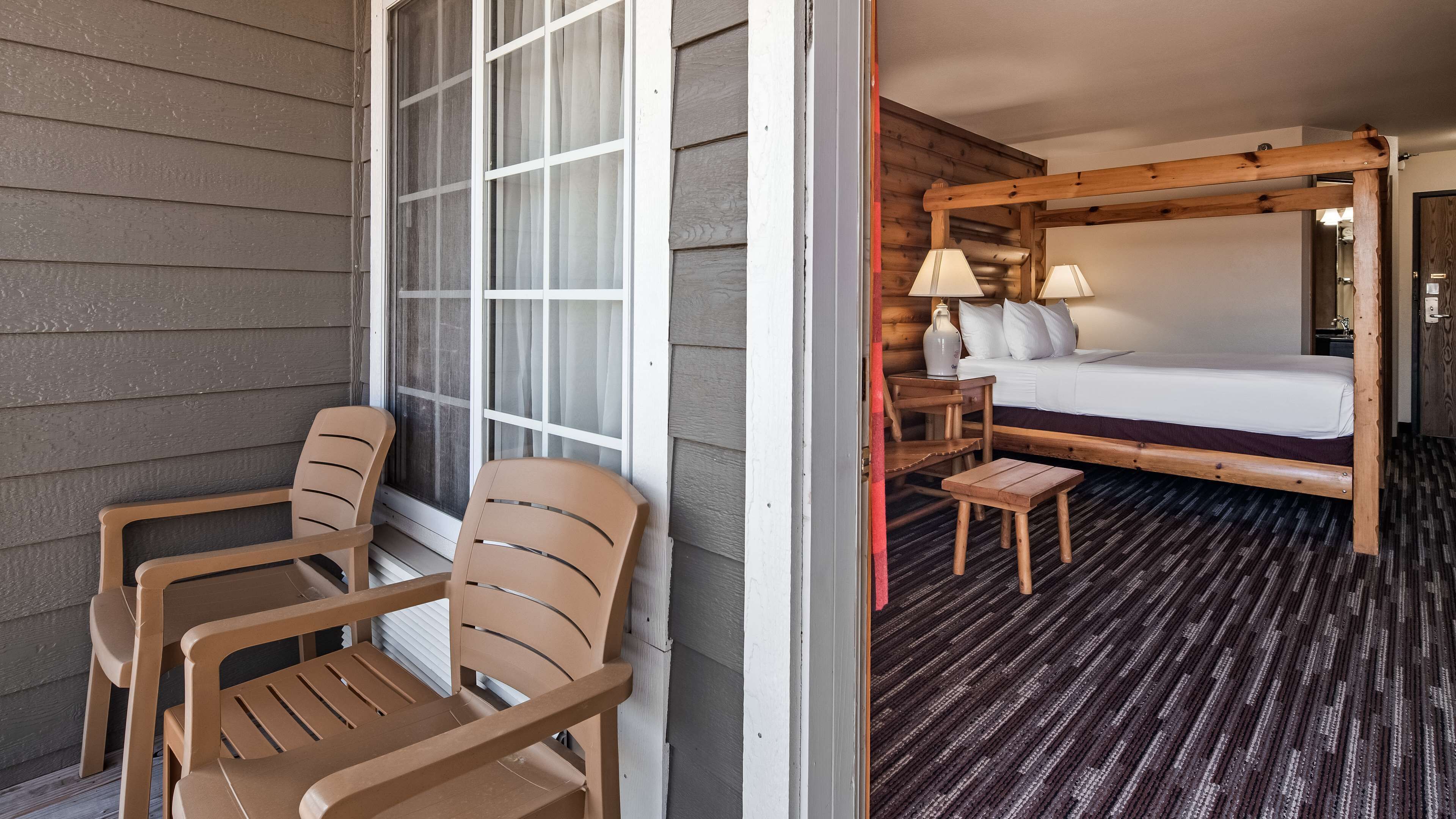 A room with a bed, a small table with lamps, and two chairs.