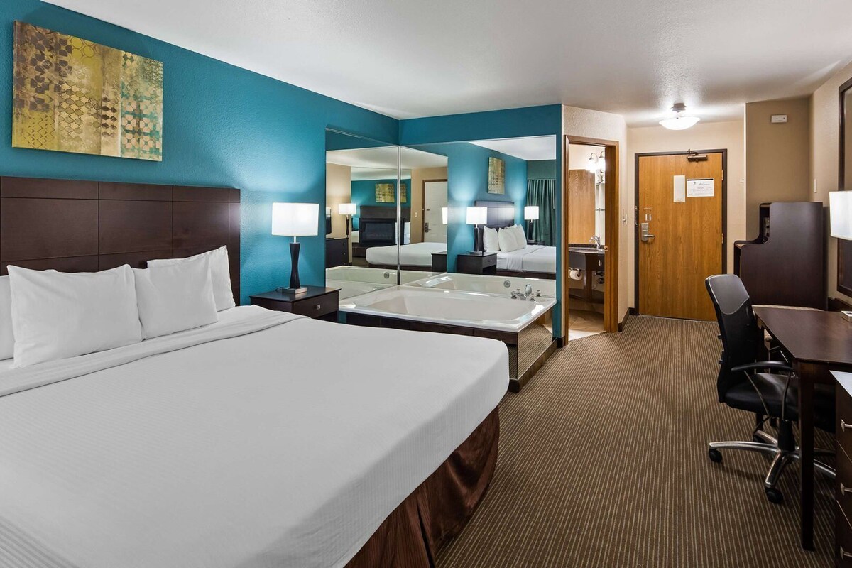 A hotel room with a large bed, a desk, a chair, a TV, a bathroom with a bathtub, and a mirror.