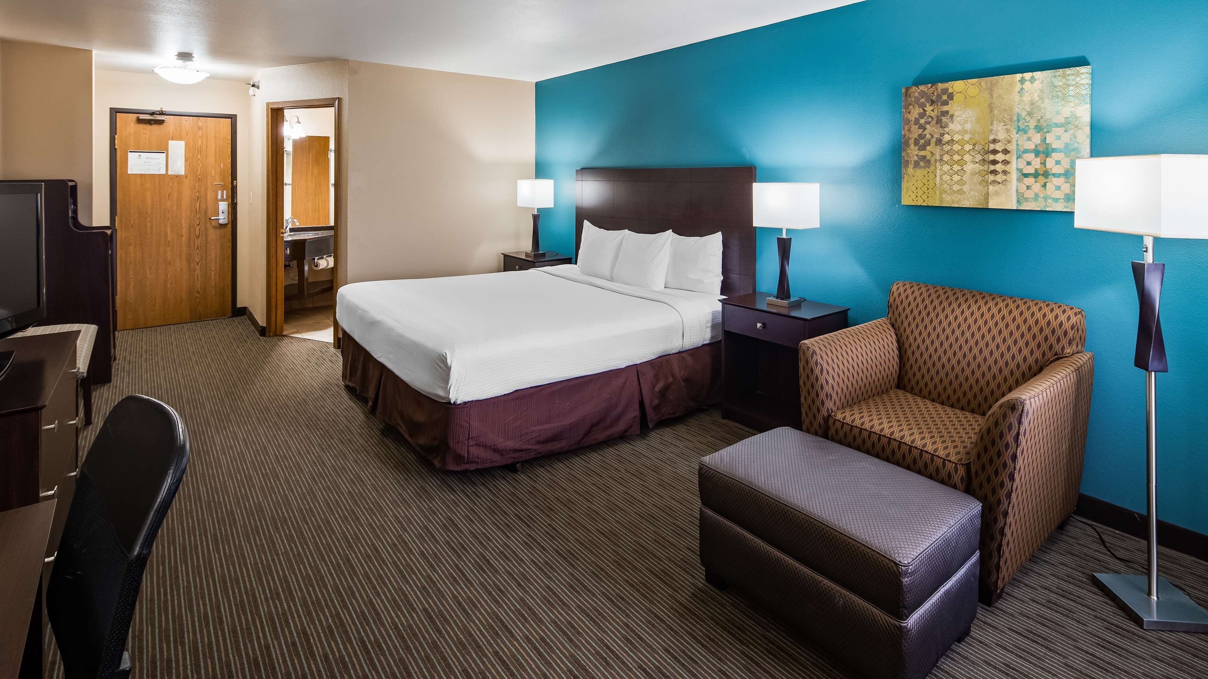 A hotel room with a large bed, two bedside tables with lamps, a sofa, a desk with a chair, and a television.
