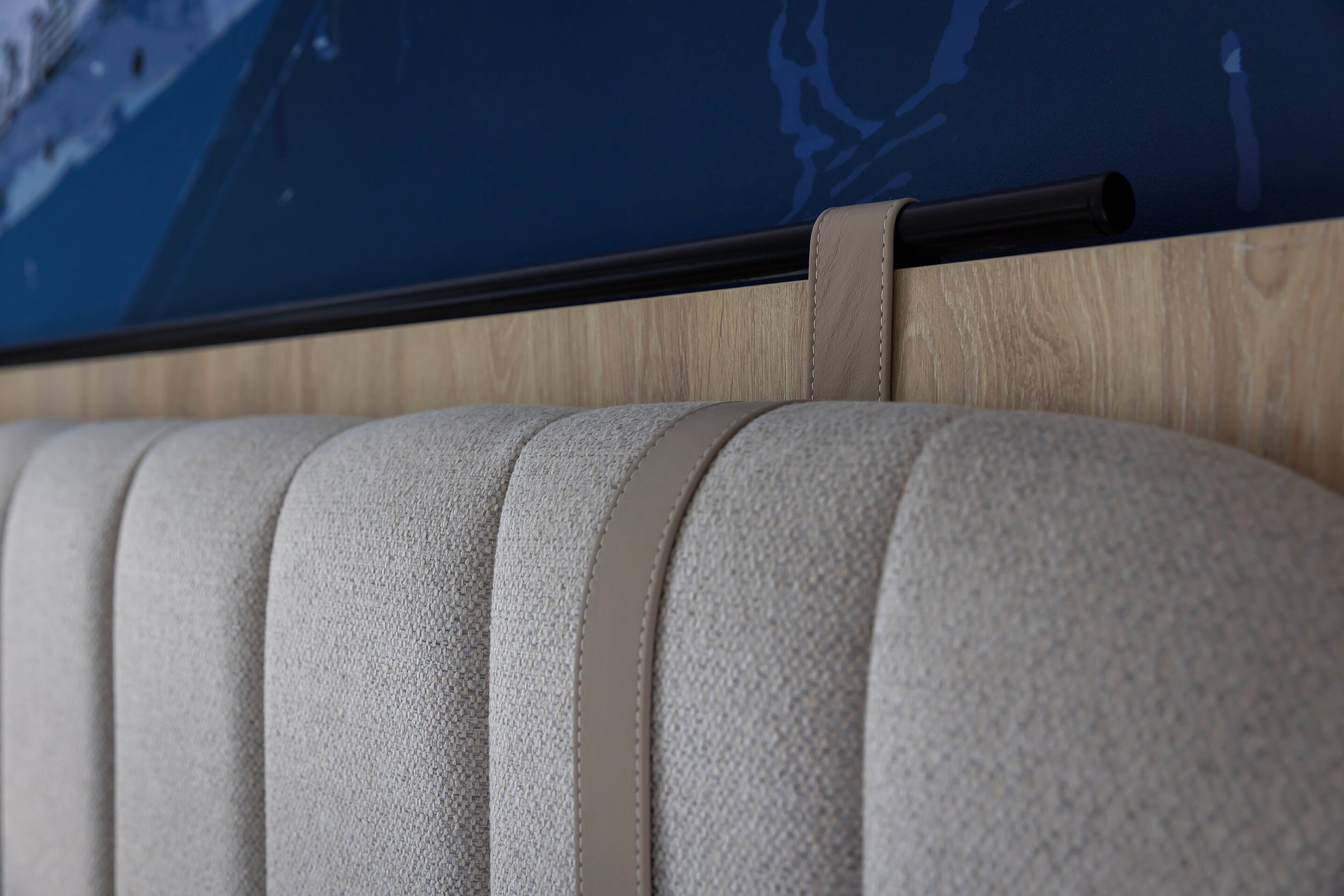 A close-up of a textured, light-colored sofa with a wooden panel and a black horizontal bar above it.