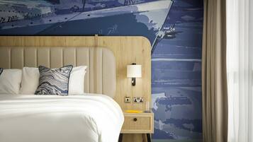 A hotel room with a large bed, a wooden headboard, a nightstand with a lamp, and a wall mural.