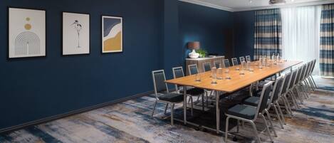 A conference room with a long table, chairs, and framed artwork on the wall.