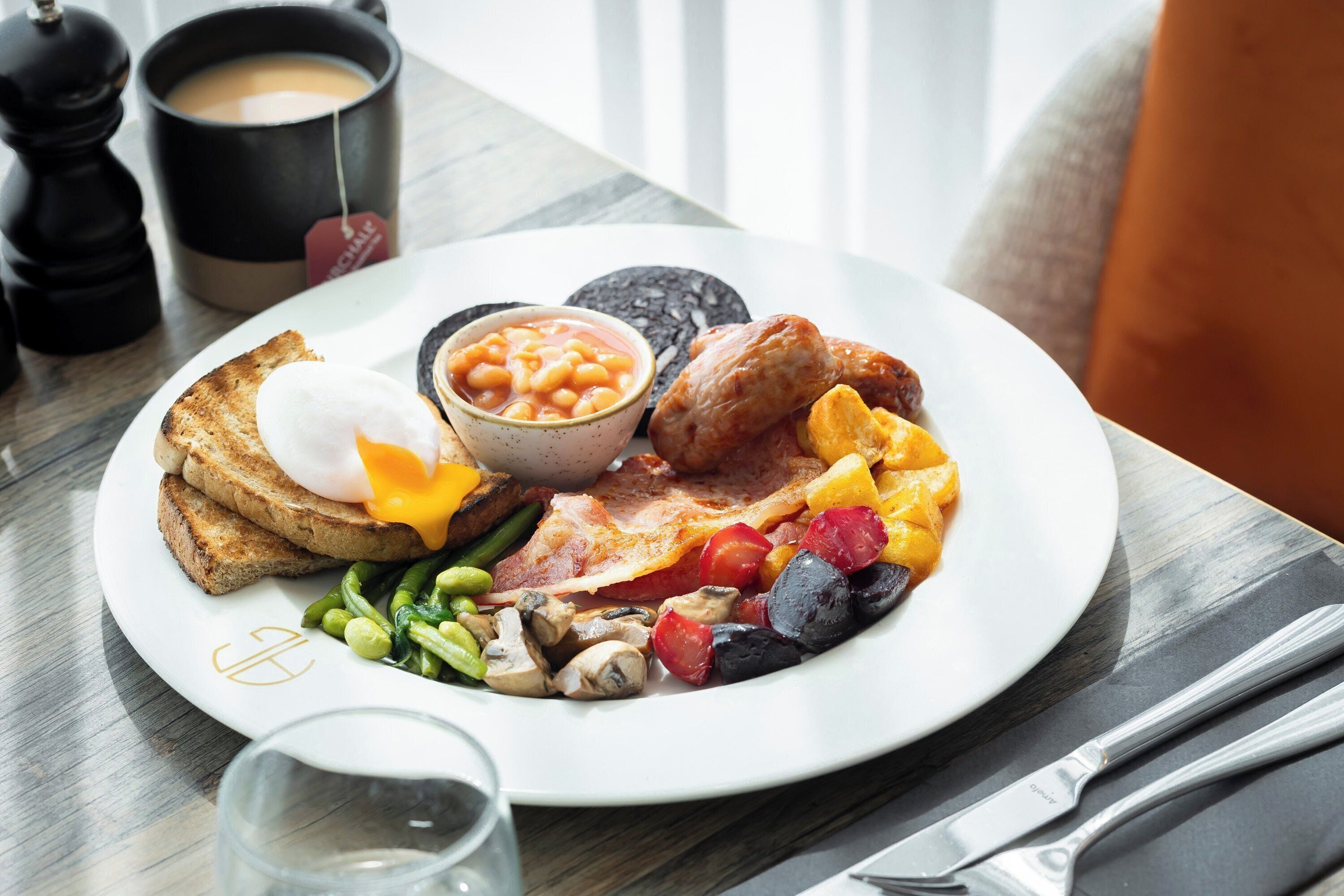 A breakfast plate with toast, eggs, beans, bacon, mushrooms, and mixed vegetables.