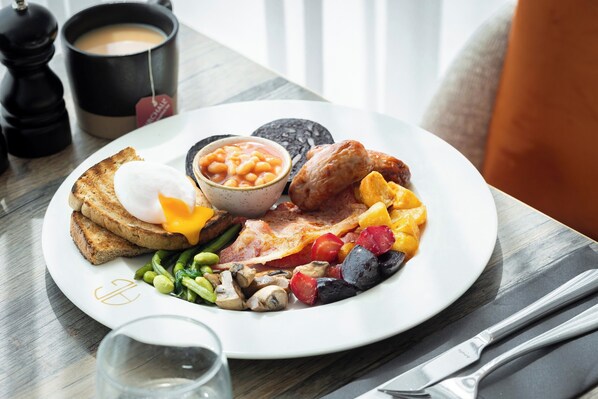 A breakfast plate with toast, eggs, beans, bacon, mushrooms, and mixed vegetables.