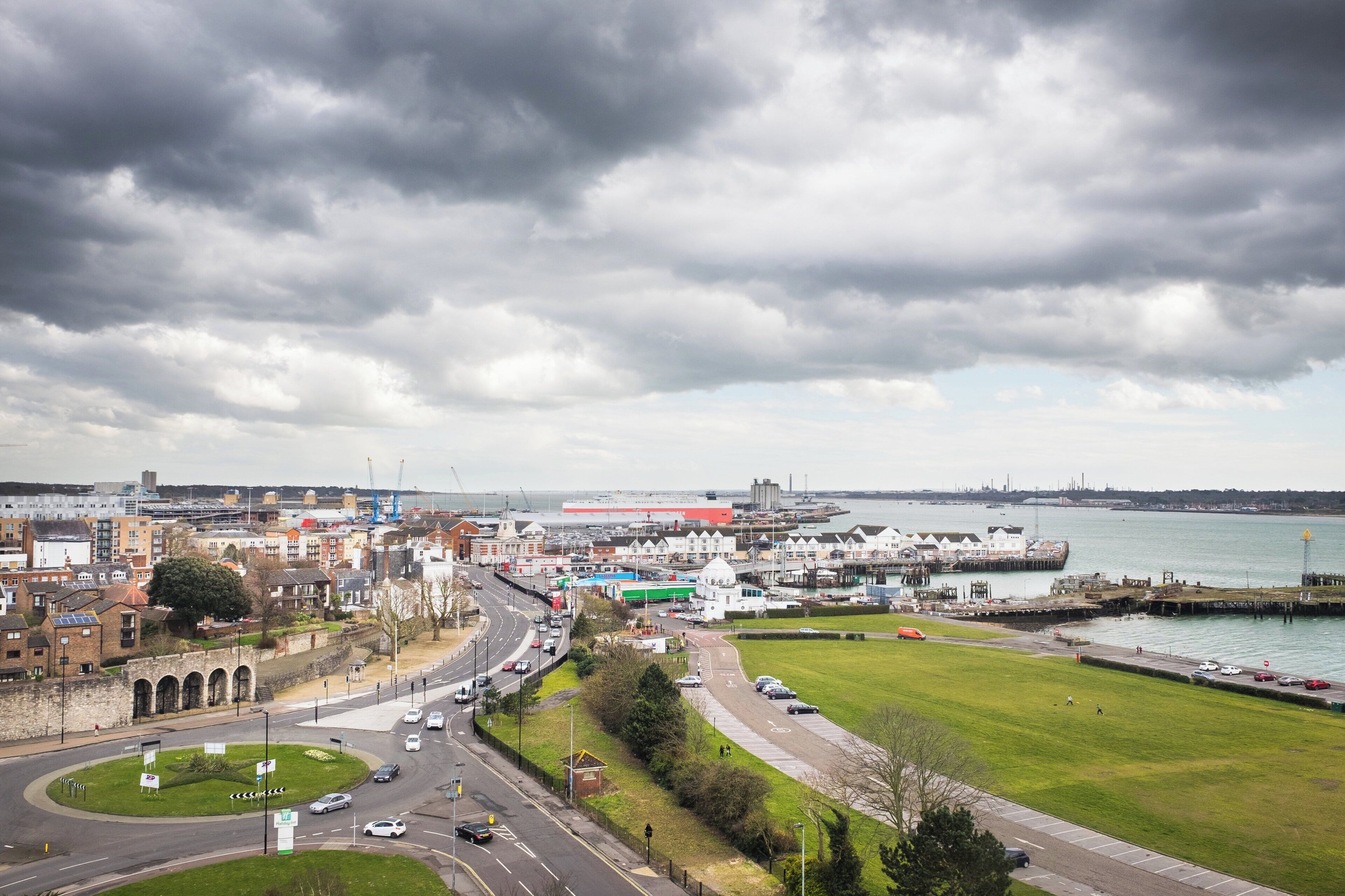 A coastal cityscape with a mix of residential and commercial buildings, a prominent port area, and a large body of water.