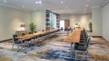 Un salón de conferencias con una larga mesa, sillas y un proyector.