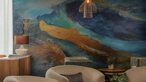Een moderne woonkamer met een groot abstract schilderij, zachte zitplaatsen, een kleine tafel en een decoratieve lamp.