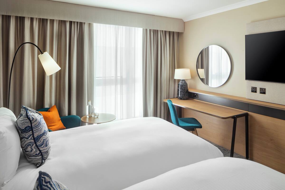 A hotel room with a large bed, a desk, a chair, a TV, a lamp, and a mirror.
