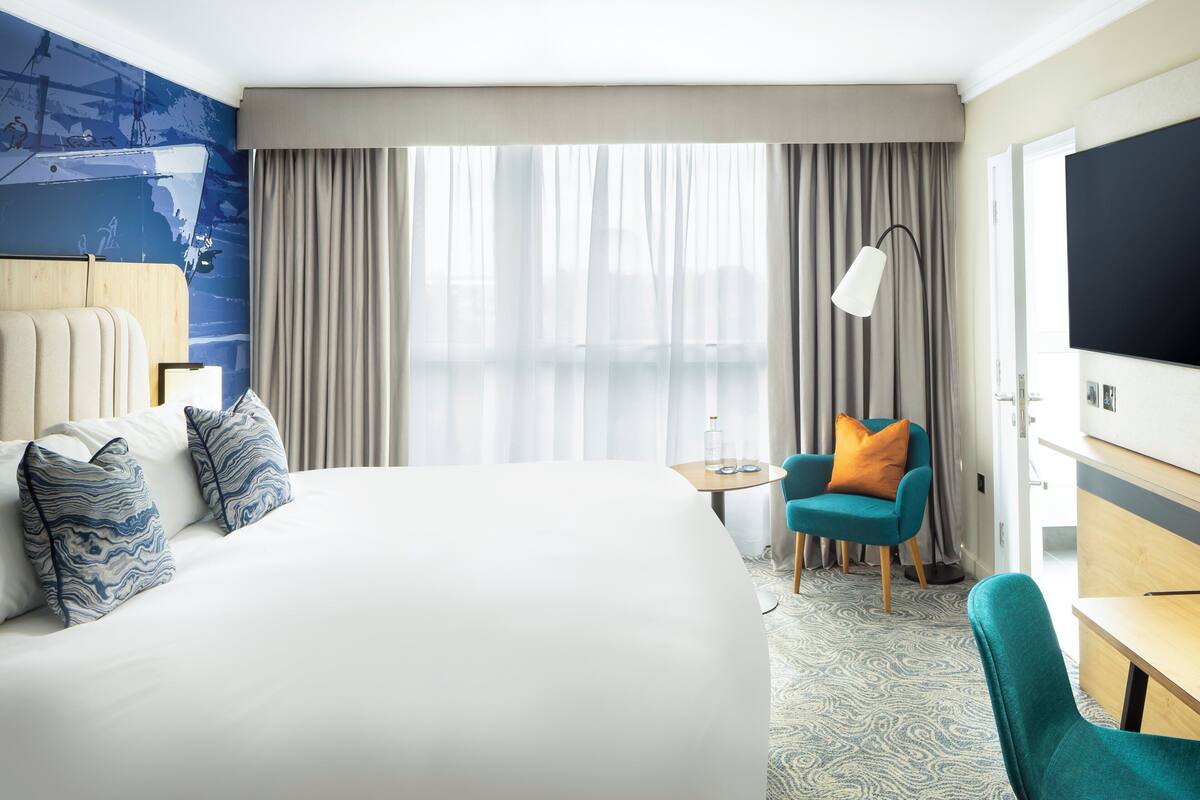 A hotel room with a large bed, a desk, a chair, and a TV.