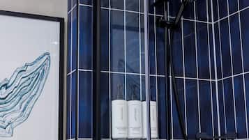 A bathroom with a glass shower enclosure, a handheld showerhead, and a framed artwork on the wall.