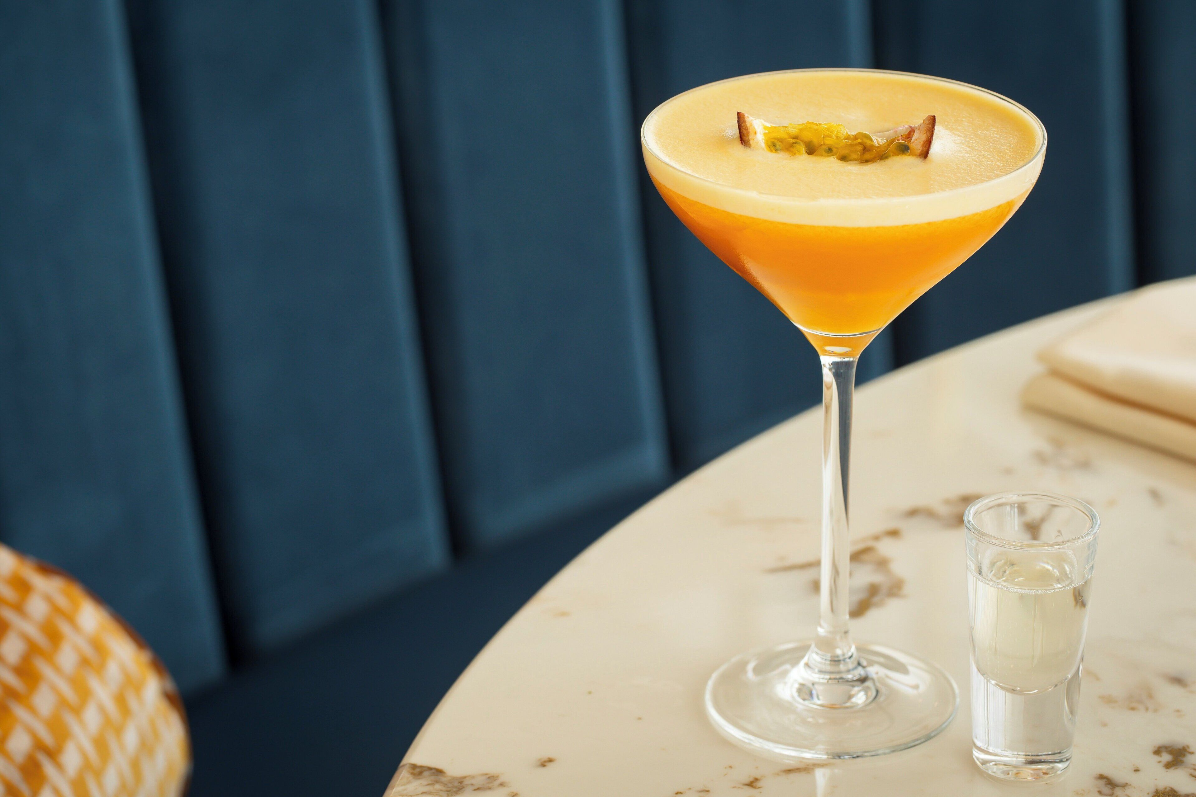 A martini glass with a yellow-orange drink and a garnish on a marble table.