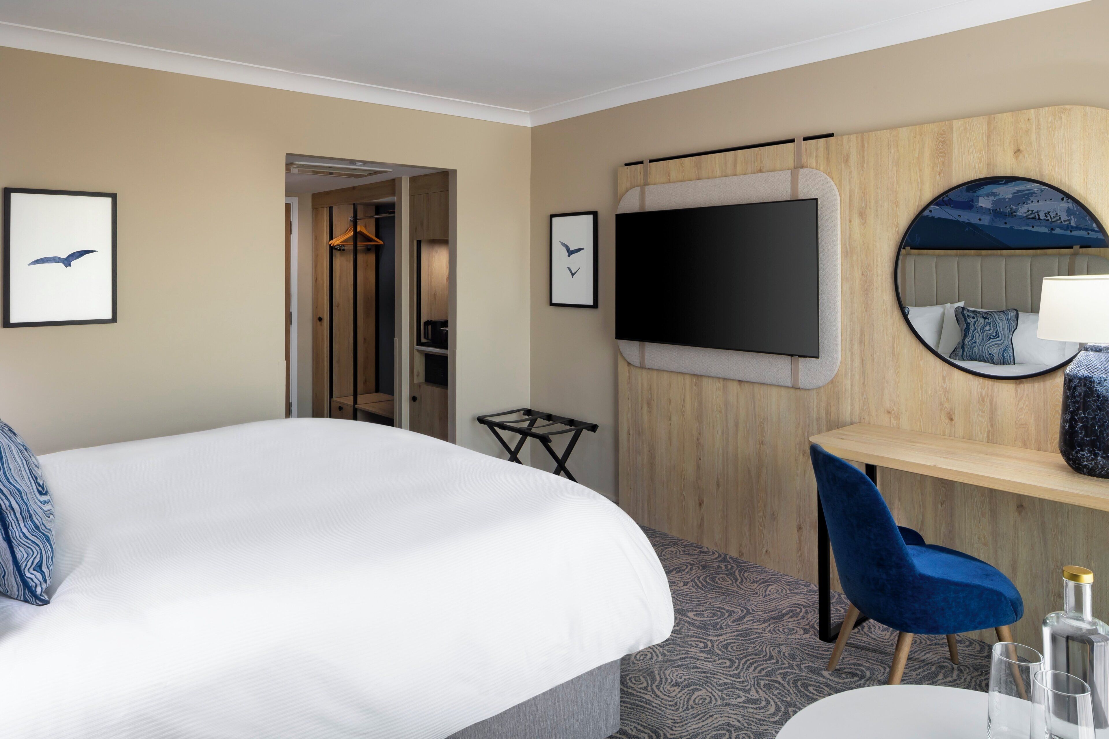 A hotel room with a large bed, a desk with a chair, a TV, and a mirror.