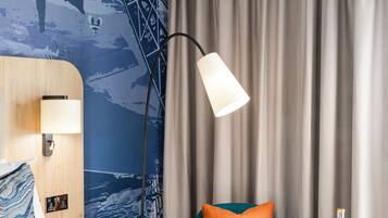 A hotel room with a bed, a desk, a chair, a lamp, and a curtain.